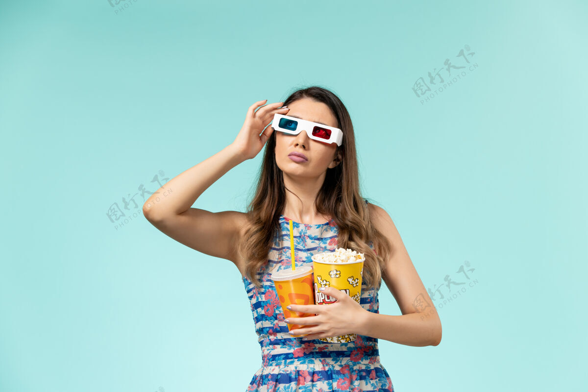 电影正面图年轻女性 带着爆米花包 戴着d墨镜在蓝色表面喝酒正面漂亮爆米花