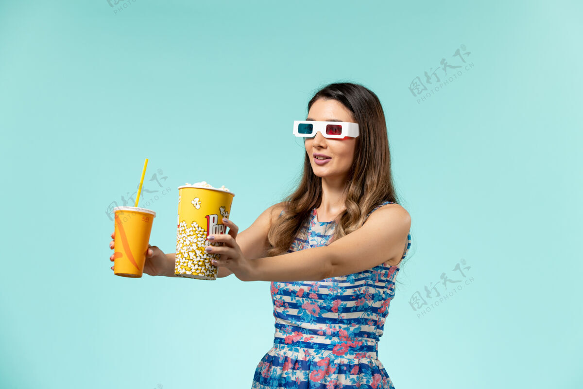 性感正面图年轻女性 带着爆米花包 戴着d墨镜在蓝色表面喝酒剧院漂亮太阳镜