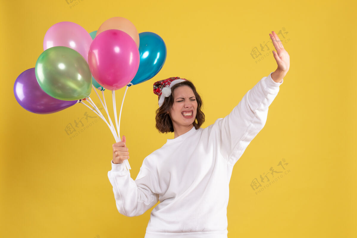 颜色正面图年轻靓女手持五颜六色的气球 对一个黄色的新年情感圣诞女人的颜色欢呼正面女人