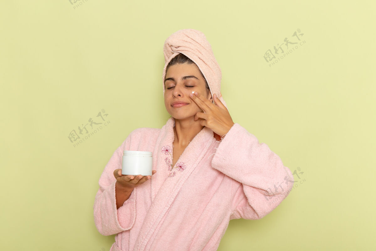 自我护理正面图穿着粉色浴袍的年轻女性在绿色表面涂面霜年轻女性长袍浴盆