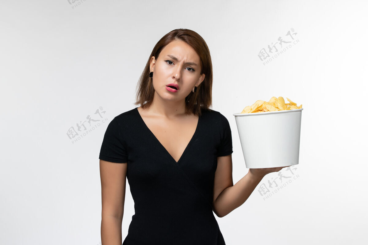 前面正面图：穿着黑色衬衫的年轻女性在白色的桌子上拿着薯片年轻的女性孤独衬衫