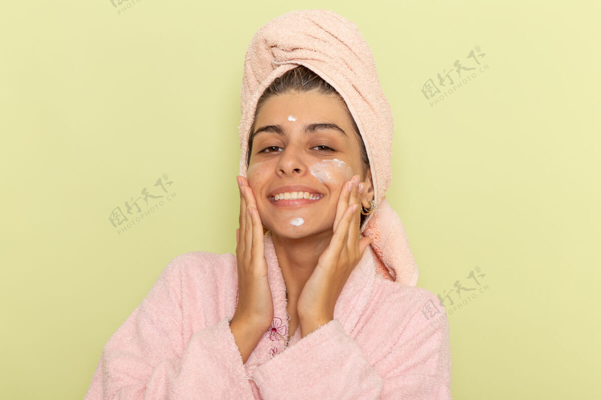 浴巾正面图穿着粉色浴袍的年轻女性在浅绿色表面涂面霜浅绿色面膜浴缸