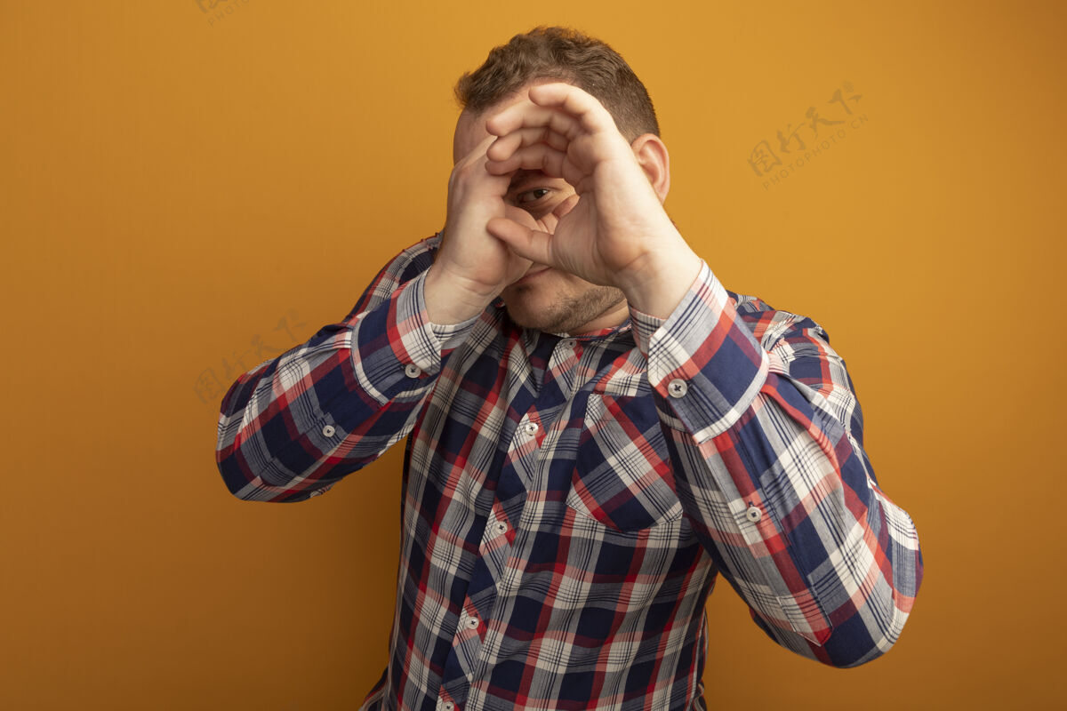 眼镜戴着眼镜和格子衬衫的男人用手指模仿站在橙色墙上的望远镜站着模仿检查