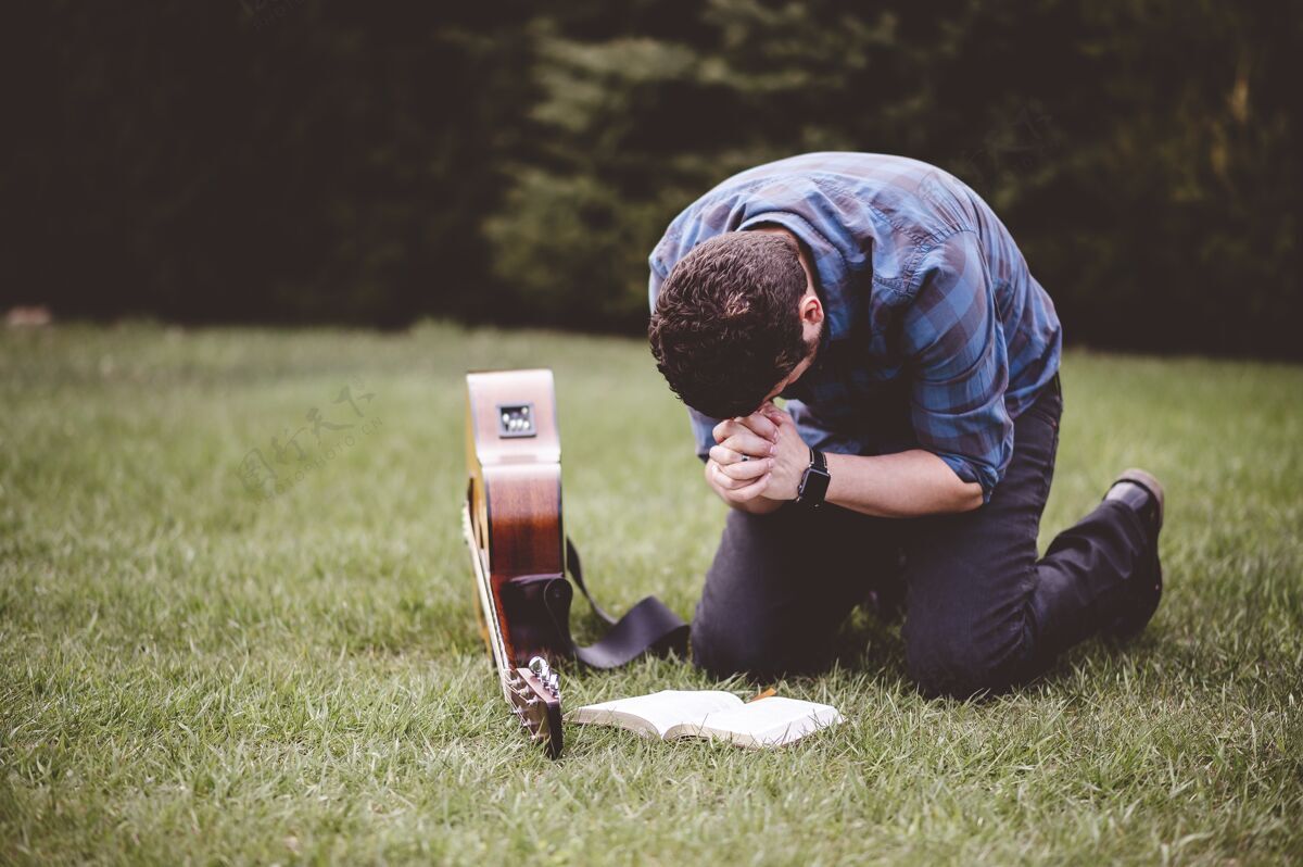 精神坐在草地上祈祷的人 身边拿着一本书和一把吉他祈祷开放传统