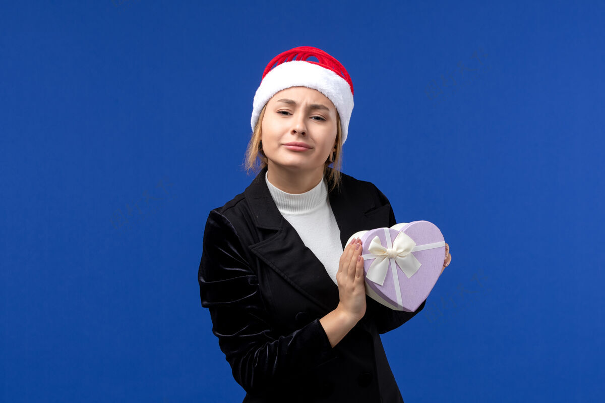圣诞节正面图年轻女士手持心形礼物在蓝色墙壁新年礼物节日生活人工人