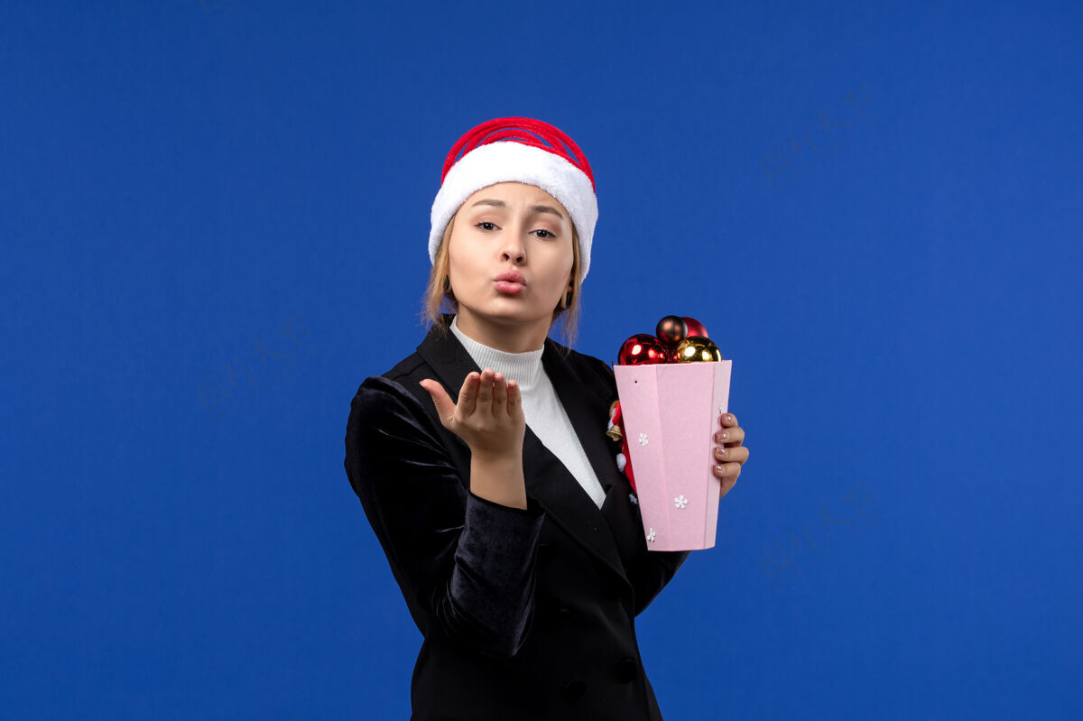 颜色前视图年轻女性手持圣诞树玩具 背景为蓝色新年假期情感色彩公司玩具人