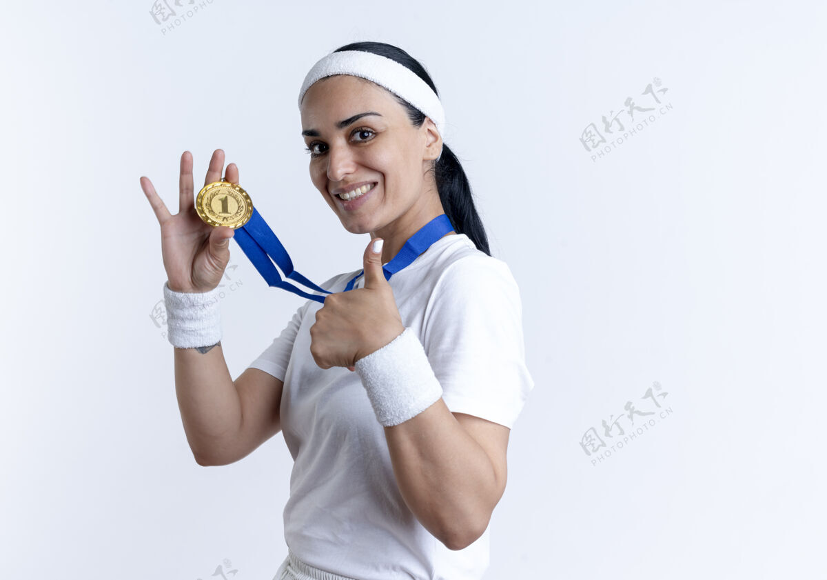 穿戴着头带和腕带 面带微笑的年轻白种人运动女性手持金牌 竖起大拇指孤立地站在空白处复制空间复制拇指太空