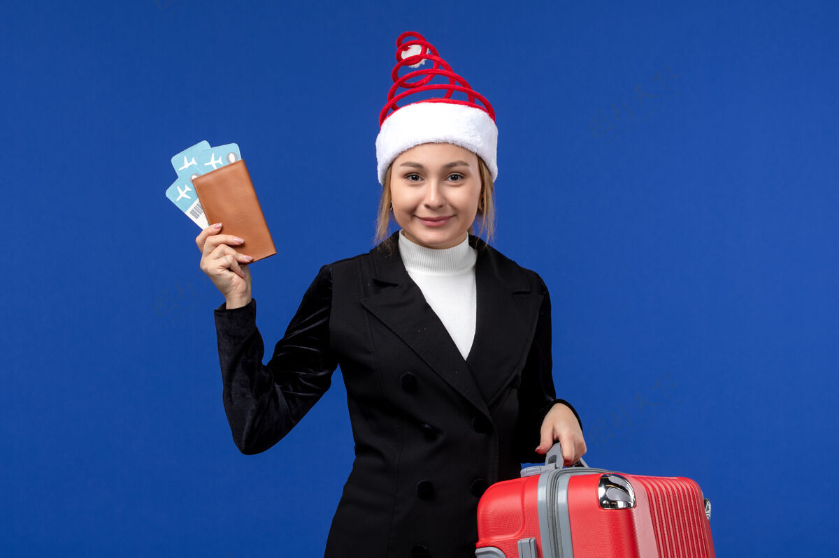 包前视图年轻女性拿着票和袋子在一个蓝色背景的女人度假西装成人女人