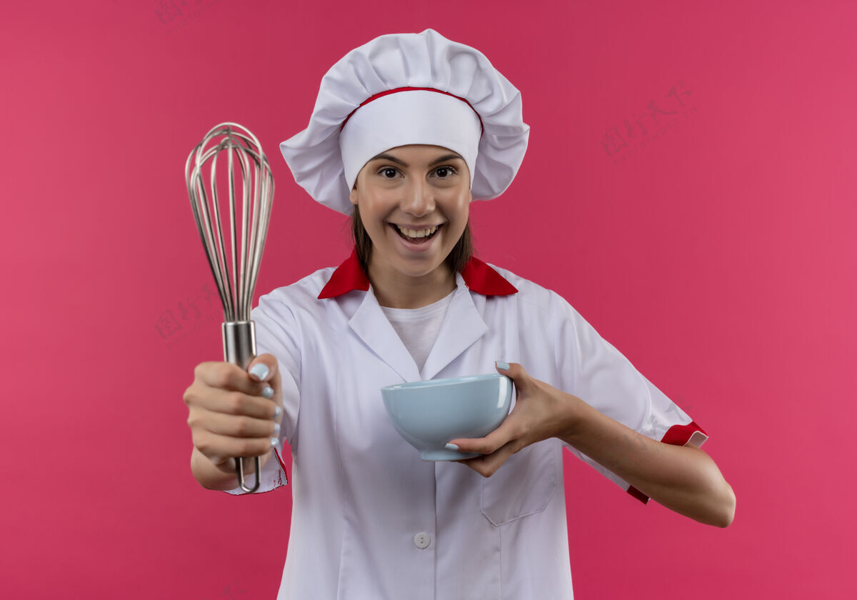 空间年轻快乐的白人厨师女孩穿着厨师制服 拿着威士忌和碗孤立地放在粉红色的空间和复制空间女孩举行年轻