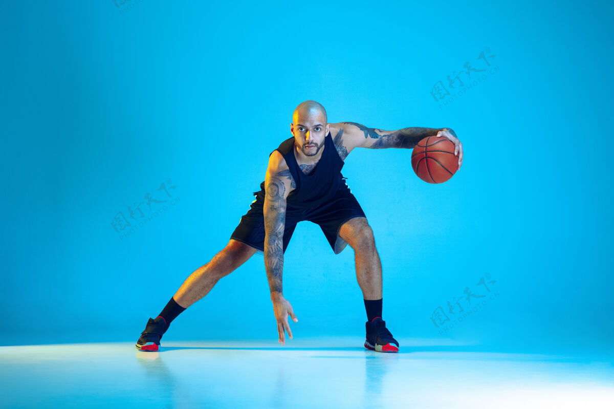 运动员年轻的篮球队员穿着运动服训练 在运动中练习 在霓虹灯下的蓝色背景下孤立运动运动的概念 运动 活力和活力 健康的生活方式运动员运动装比赛