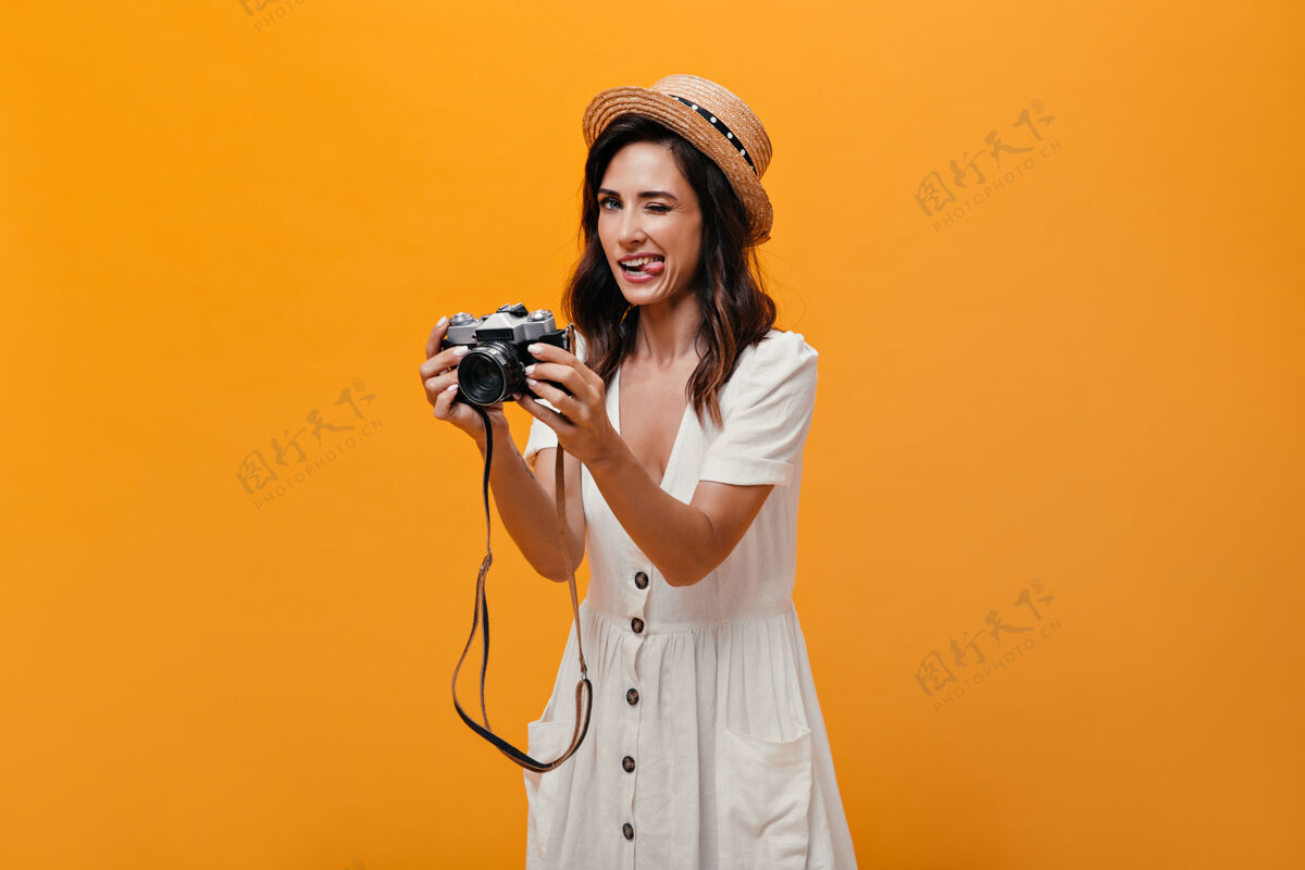 女孩穿着白色连衣裙 戴着帽子的漂亮女孩露出舌头 拿着复古相机滑稽的女人穿着夏装 短发摆姿势深色休闲圆点