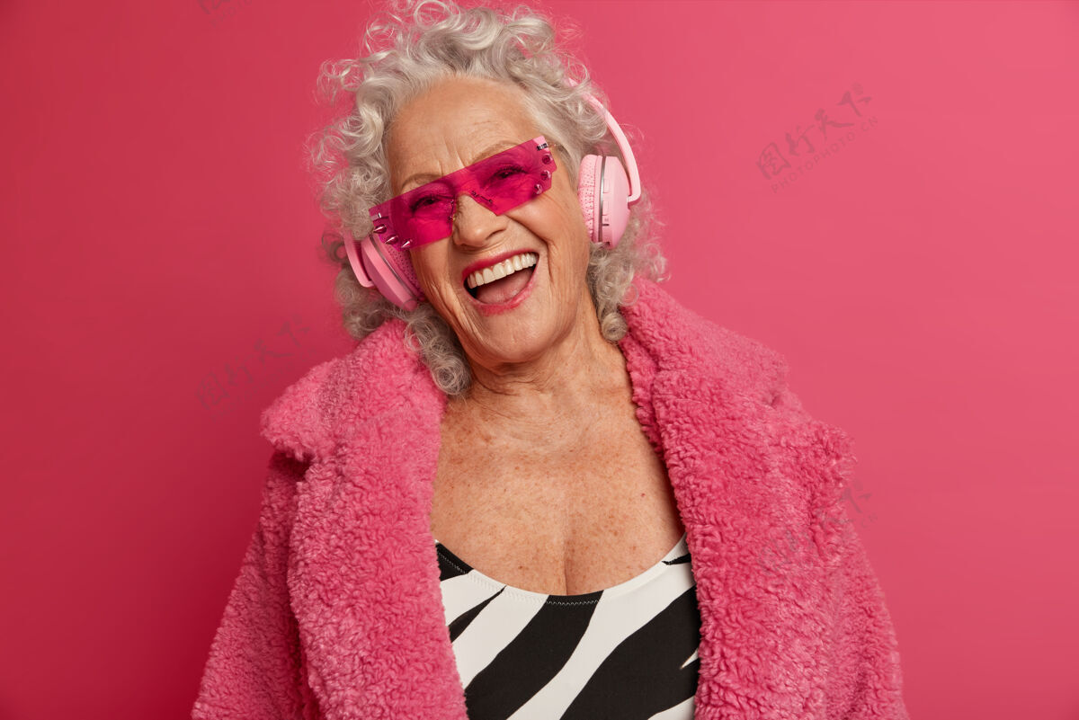 外套穿着粉色紧身衣和外套 满脸皱纹的时尚老奶奶的特写照片退休老年人耳机