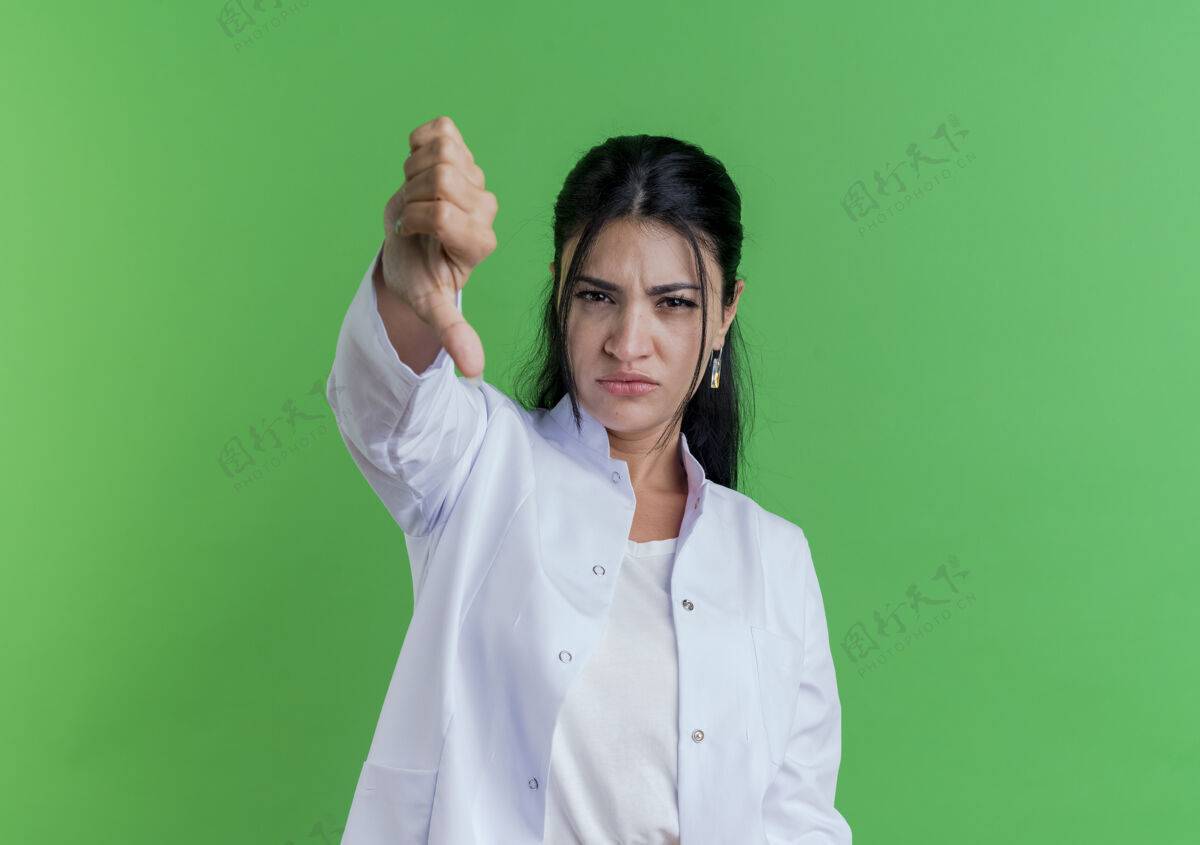 年轻未出狱的年轻女医生穿着医用长袍 拇指朝下 隔离在绿色的墙上 留有复印空间拇指看穿