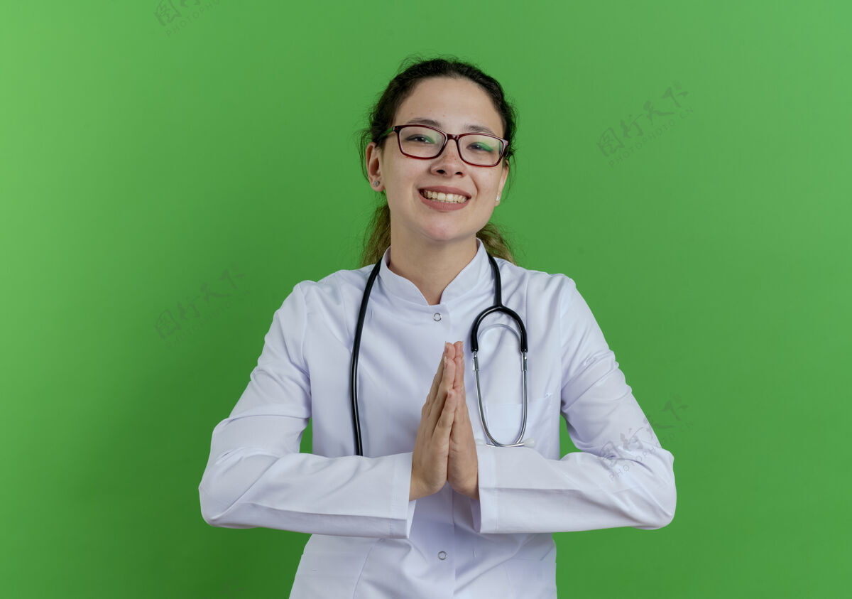 保持面带微笑的年轻女医生 穿着医用长袍 戴着听诊器 戴着眼镜 在绿色的墙壁上保持双手的隔离 还有复印空间长袍医疗医生