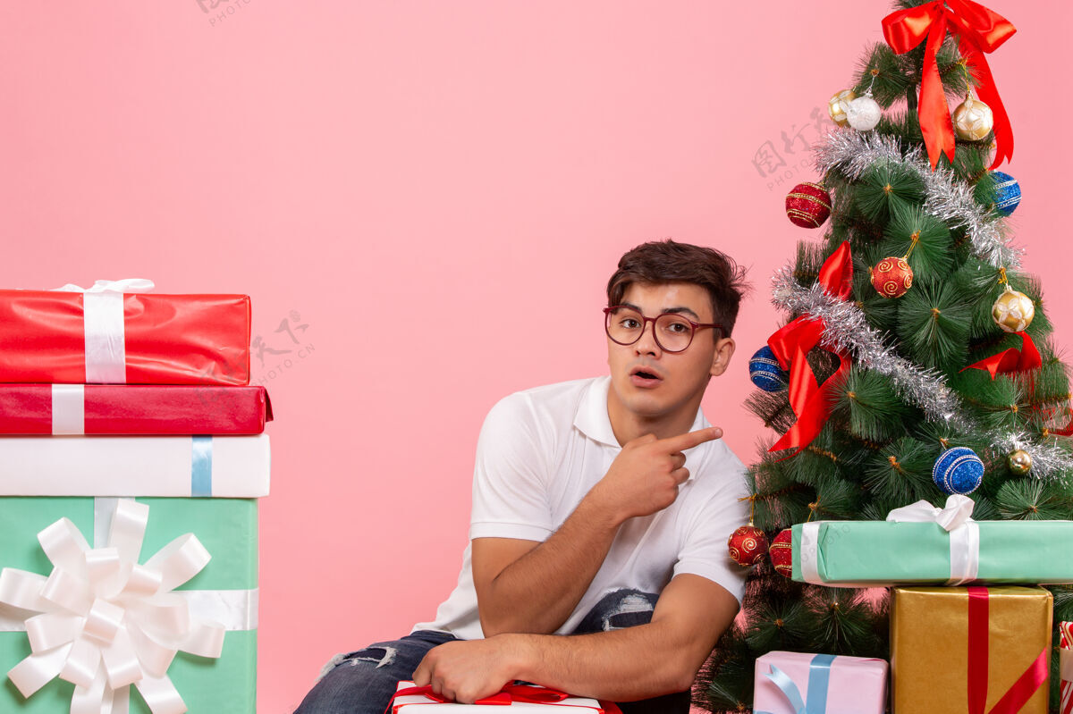 年轻人前视图年轻人周围的礼物和粉红色背景上的圣诞树房子礼物风景