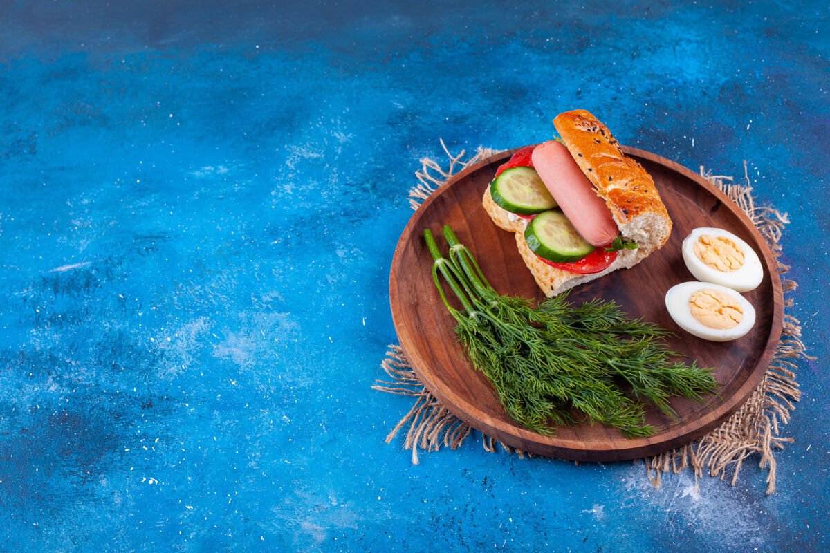 切片木制的香肠三明治 蓝色表面有莳萝和鸡蛋鸡蛋美味莳萝