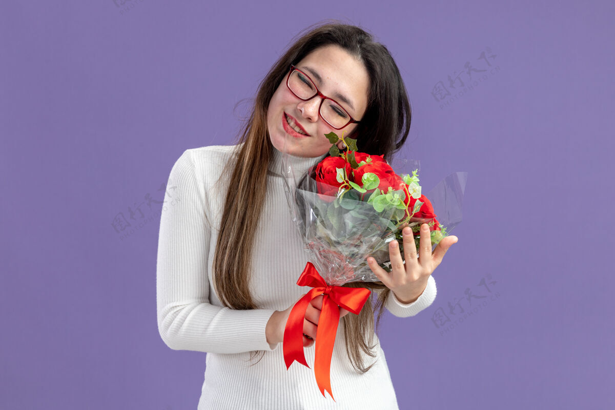 日子穿着休闲服的年轻美女手持一束红玫瑰快乐而积极的心情感恩的情人节概念站在紫色的墙上谢谢玫瑰女人