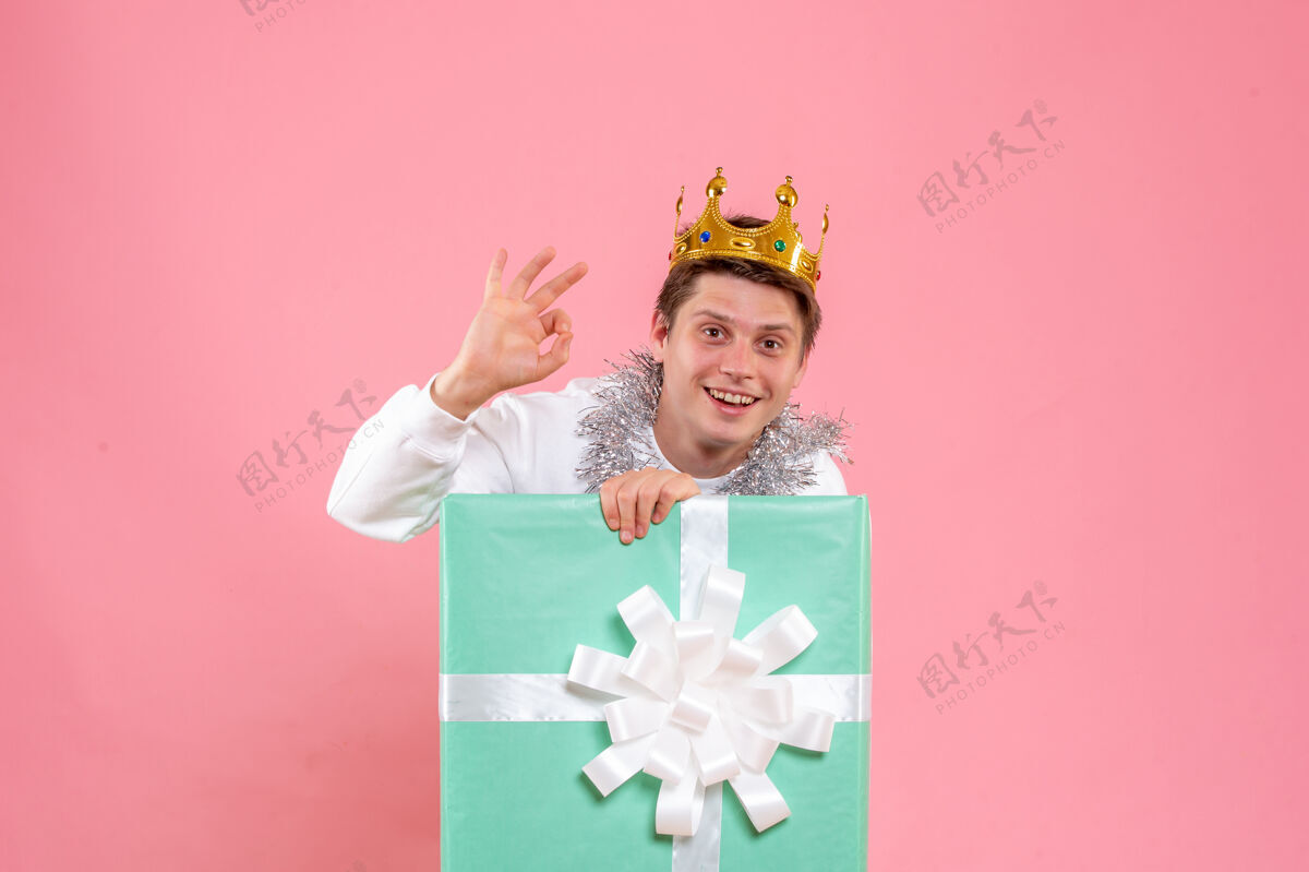 圣诞正面图：年轻男性在粉色背景上戴着皇冠粉色礼物皇冠