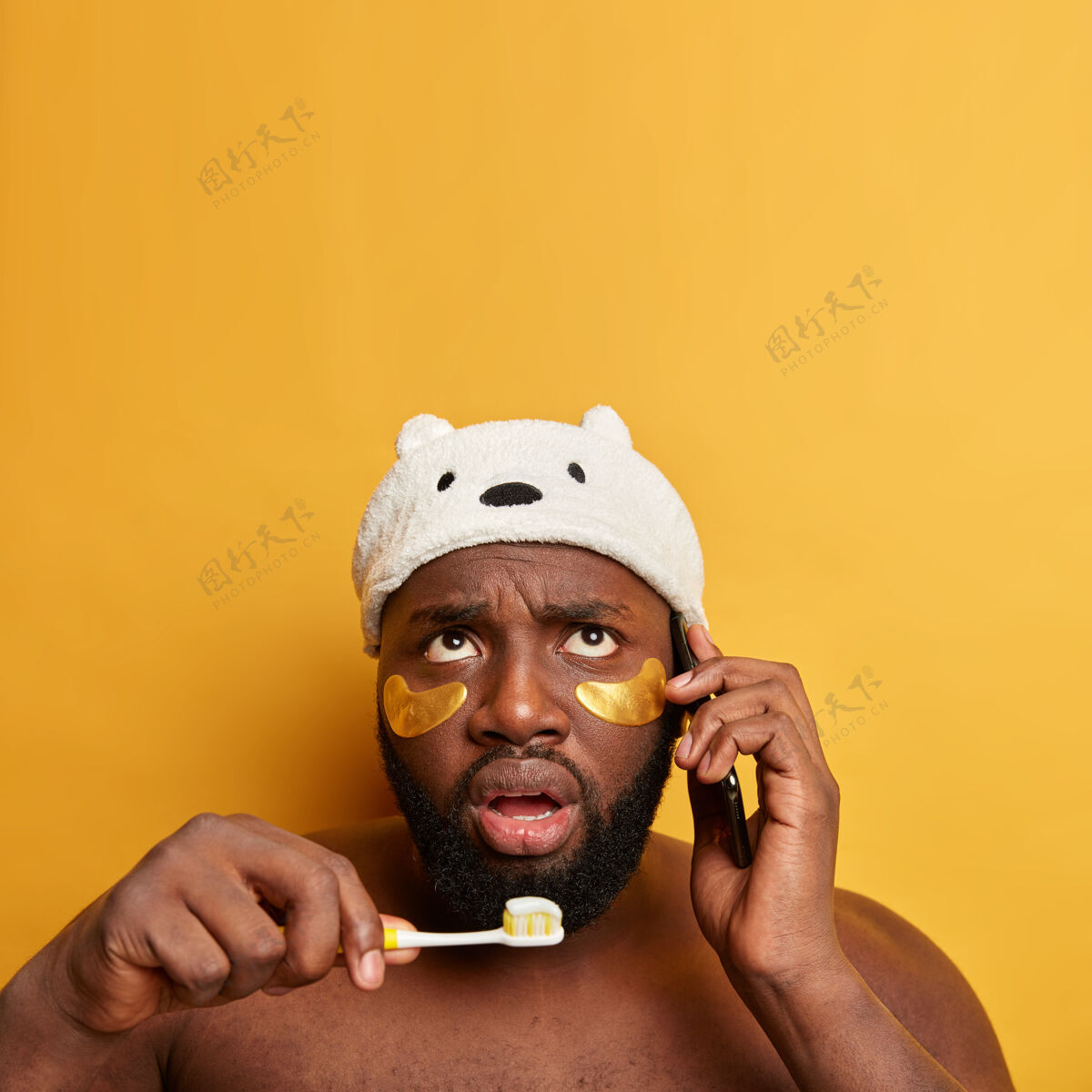 卫生困惑的非洲男人正忙着工作 有电话交谈 刷牙 眼睛下戴着胶原蛋白贴片电话口腔成人
