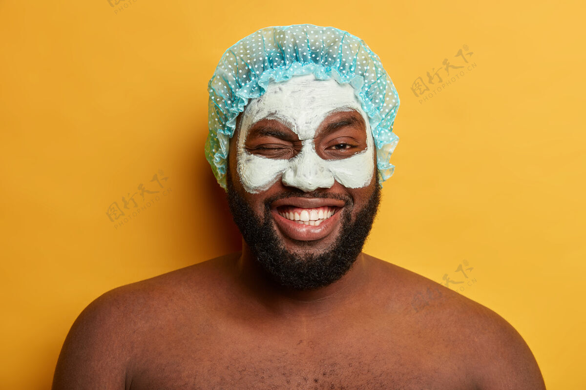 高兴搞笑正面黑皮肤男人眨眼 淋浴后敷抗衰老面膜 戴防护帽健康积极皱纹