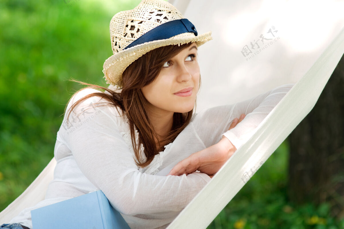 放松年轻女人拿着书在吊床上放松吊床休息休闲活动
