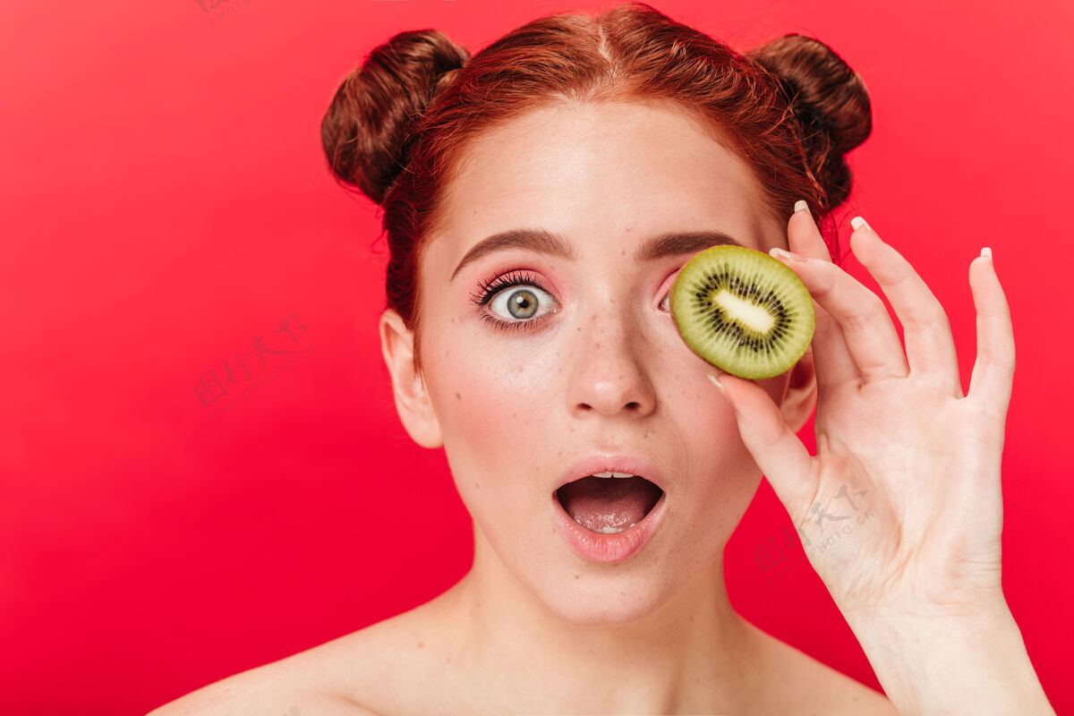 女孩拿着猕猴桃的姜汁女孩震惊了摄影棚拍摄了一个在红色背景上隔离异国水果的惊讶女人甜美欢呼食物