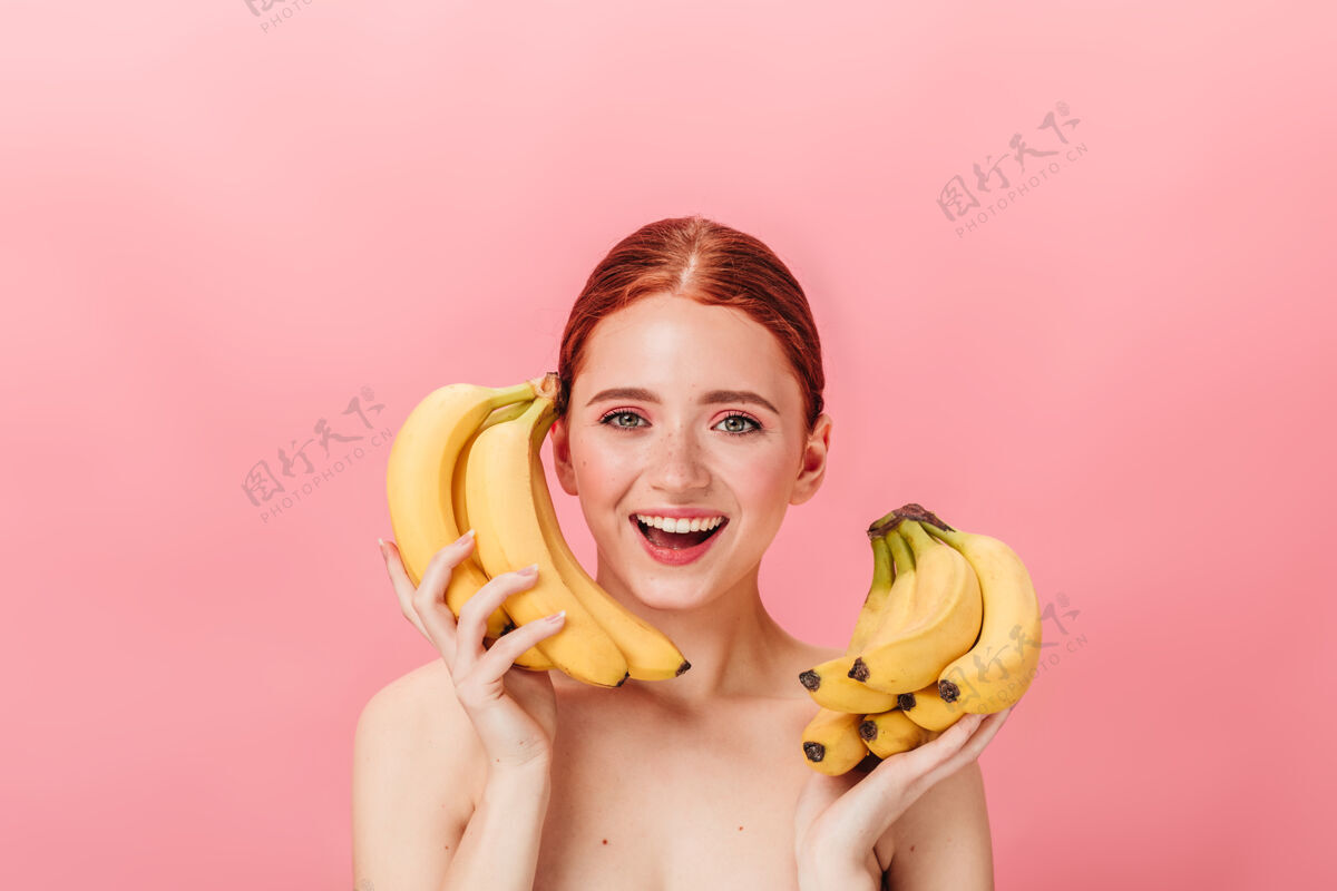 香蕉令人惊叹的姜汁女孩与香蕉的正面视图摄影棚拍摄的快乐裸体女子手持粉红色背景上的热带水果微笑裸体女人