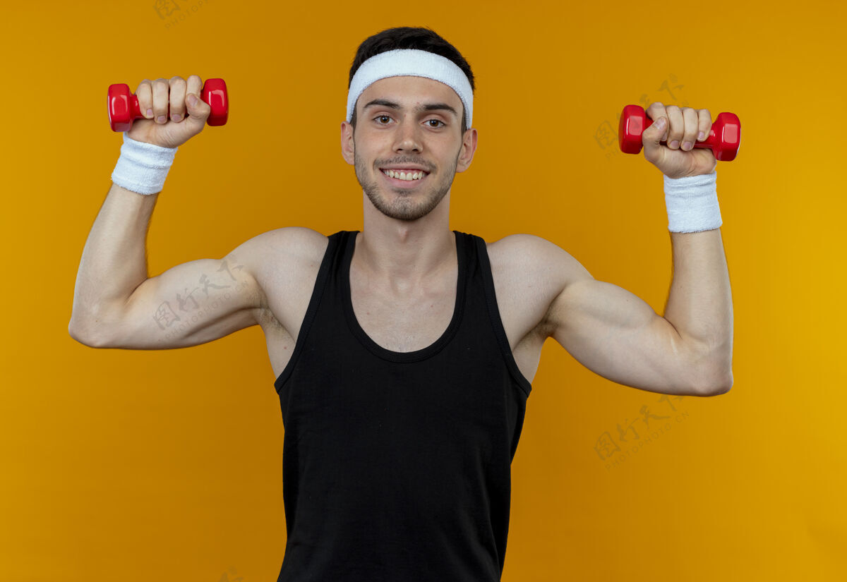 男人戴着头巾的年轻运动型男子 带着哑铃在橘子上微笑着锻炼身体年轻头带运动