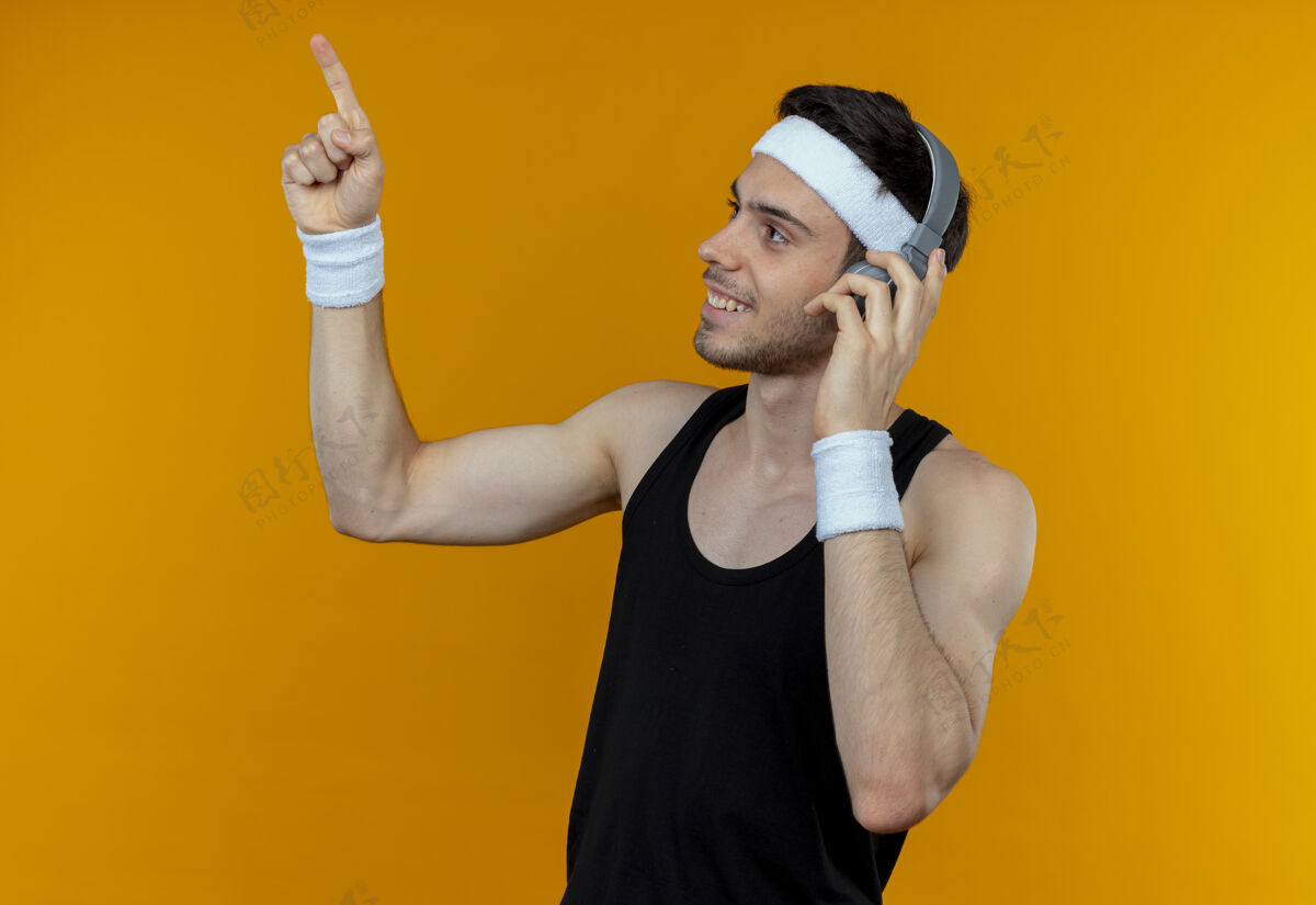 运动戴着头戴式耳机的年轻运动型男子一边看一边用手指指着橙色微笑指着头带向上