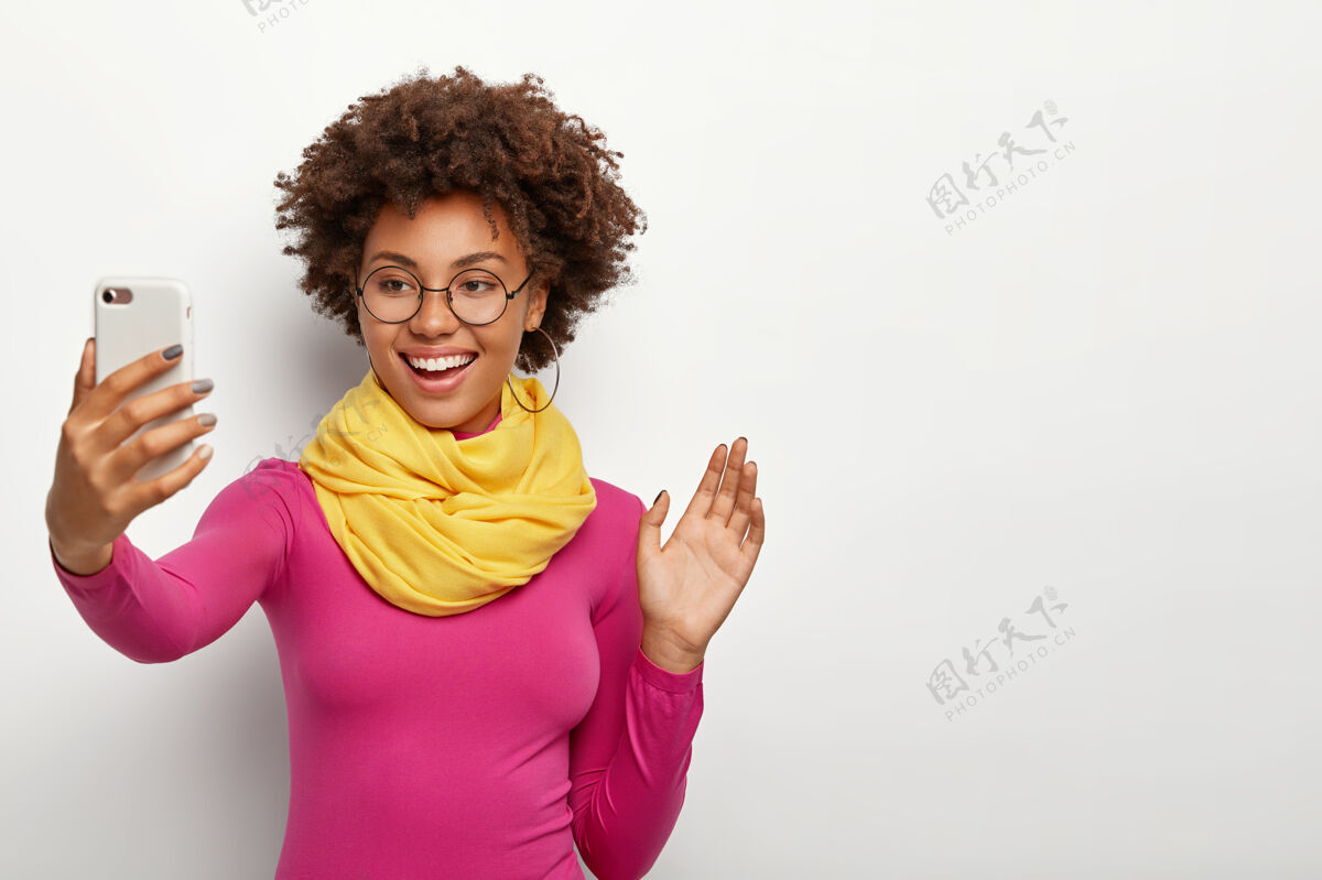 通信笑容可掬的非洲裔女孩 清爽的头发 在智能手机的摄像头里挥动手掌 打视频电话现代互联网音频