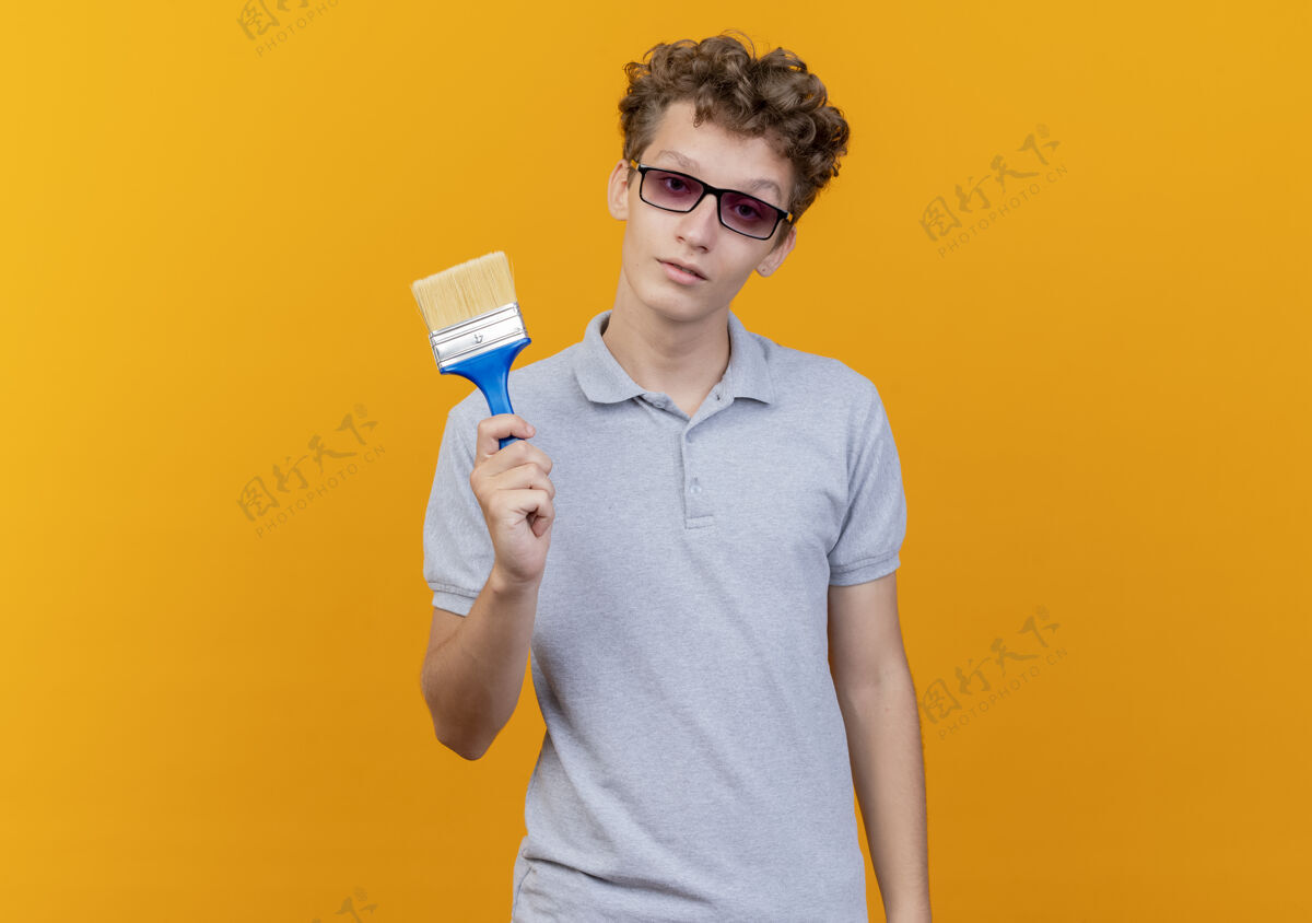 站一个戴着黑眼镜的年轻人穿着灰色马球衫 脸上带着严肃的油漆刷 而不是橙色显示看橙色