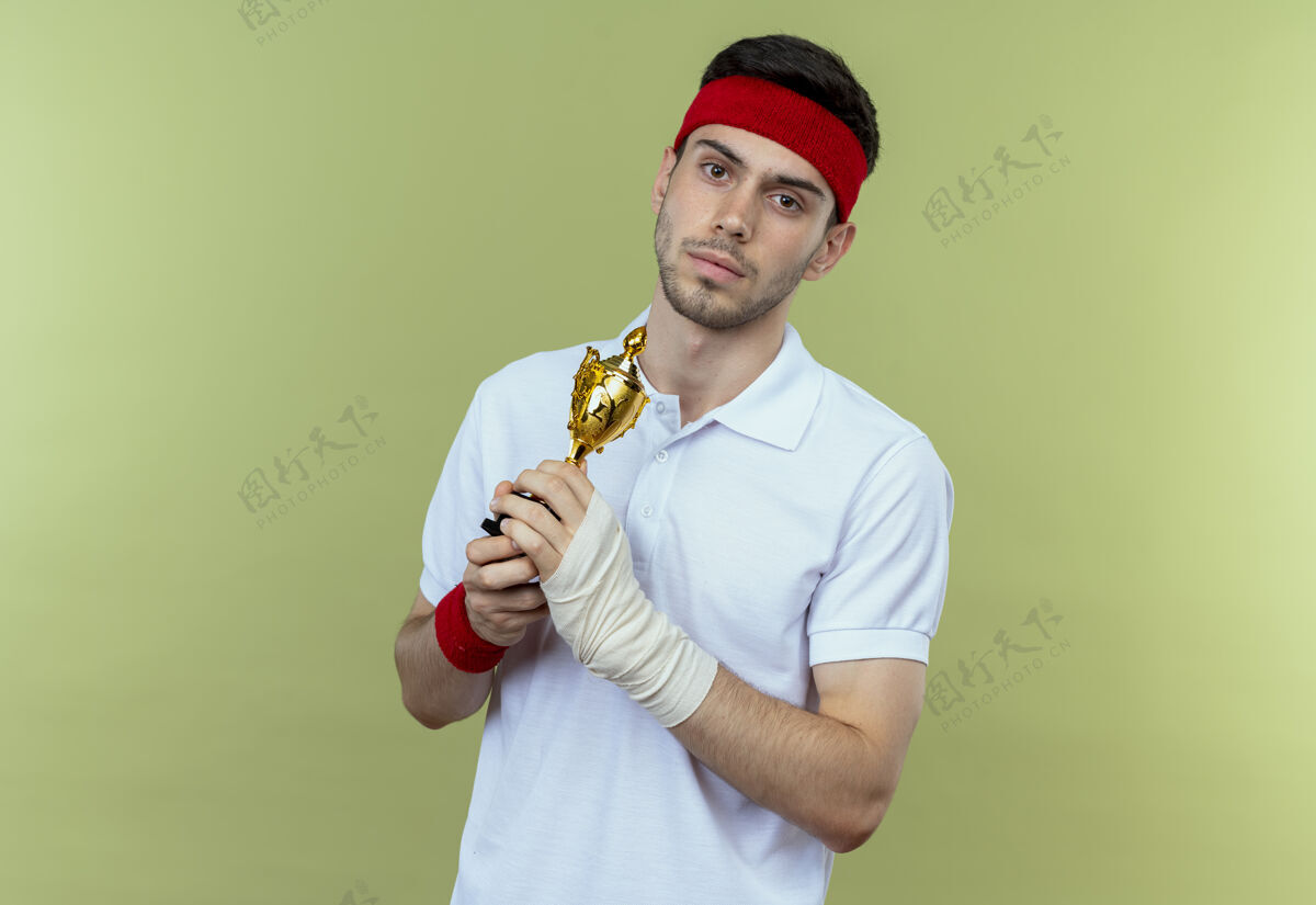 脸戴着头巾的年轻运动型男子举着他的奖杯 严肃的脸站在绿色的墙上看着运动严肃