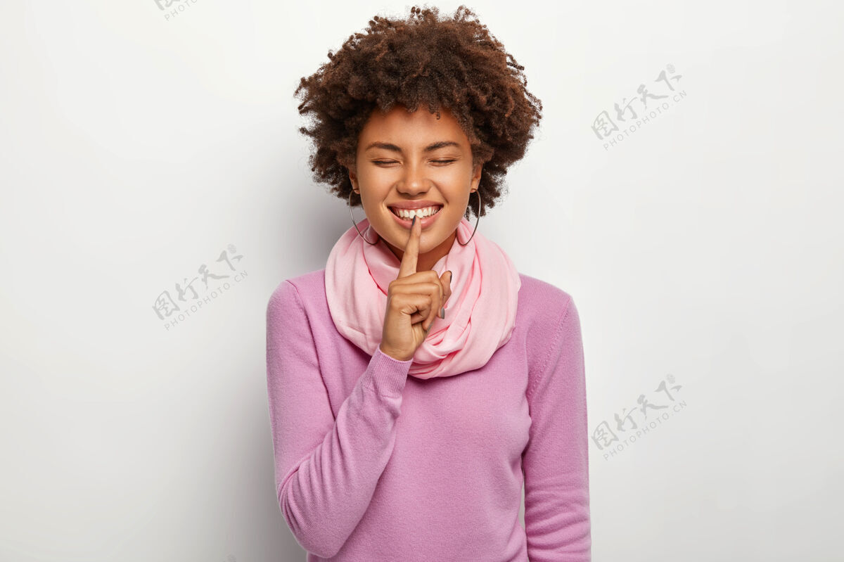 快乐快乐的女人做沉默的手势 把食指放在嘴唇上 高兴地和最好的朋友分享愉快的秘密 穿着紫色休闲套头衫沉默肖像快乐