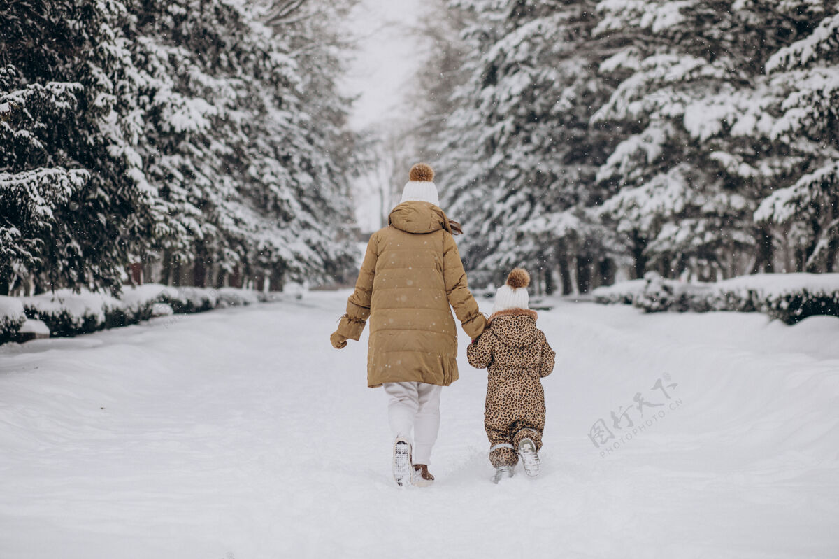 霜冻妈妈和女儿在满是雪的公园里玩下雪欢呼玩耍