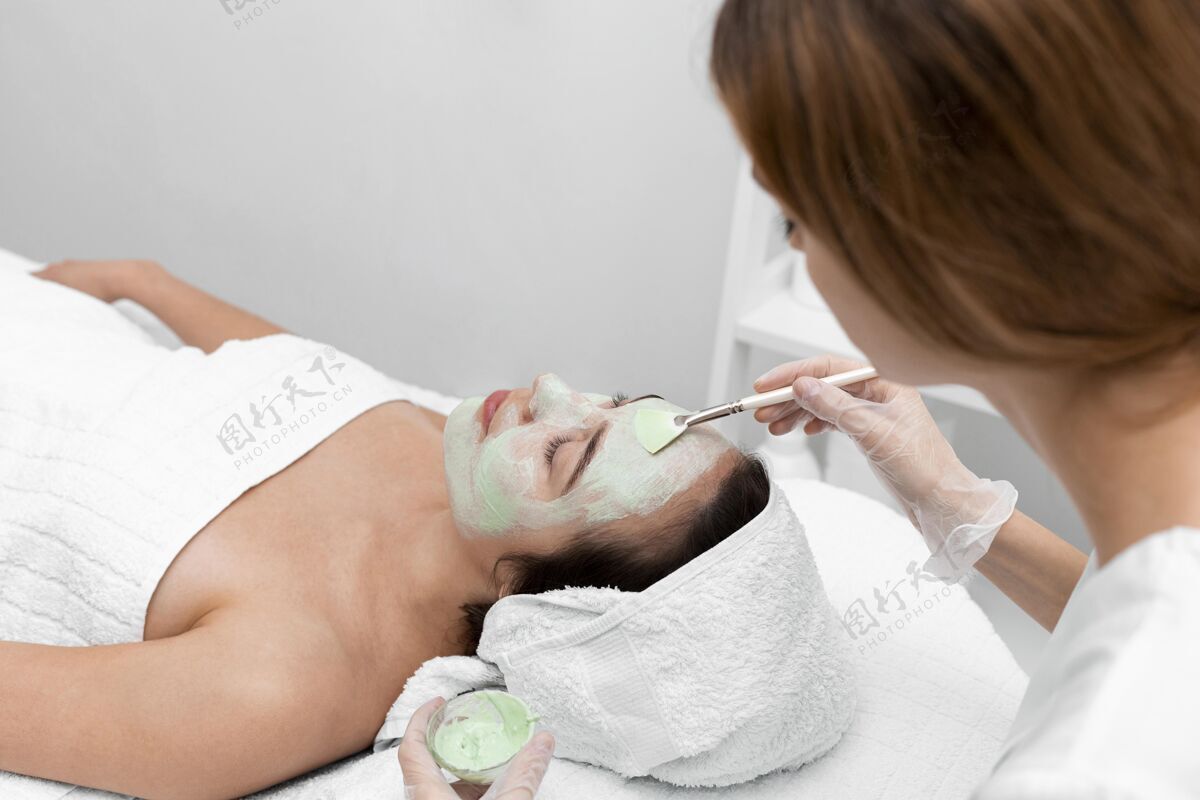 女人美容师给女性客户敷面膜涂抹美容治疗化妆品