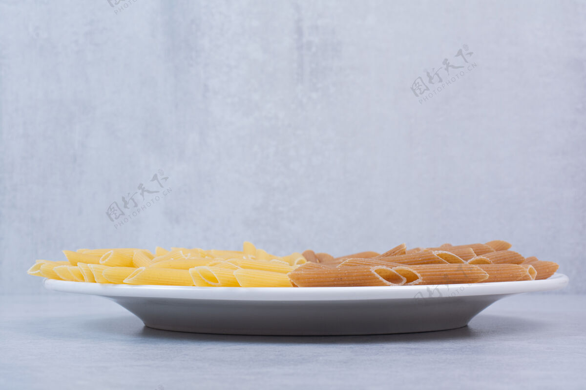 盘子在白色盘子里放一堆棕色和黄色的意大利面烹饪干的生的