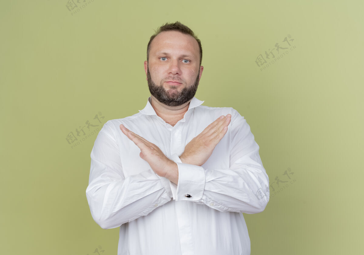 交叉留着胡子的男人穿着白衬衫 严肃地做着停止的手势 双手交叉站在轻墙上停止脸站