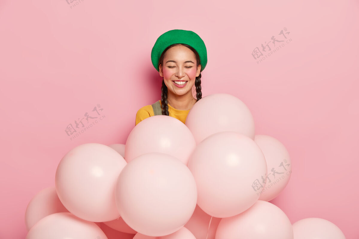 化妆面带微笑的女人 表情开朗 闭上眼睛不让人高兴 戴着绿色贝雷帽 站着充气的氦气球派对欢呼姿势