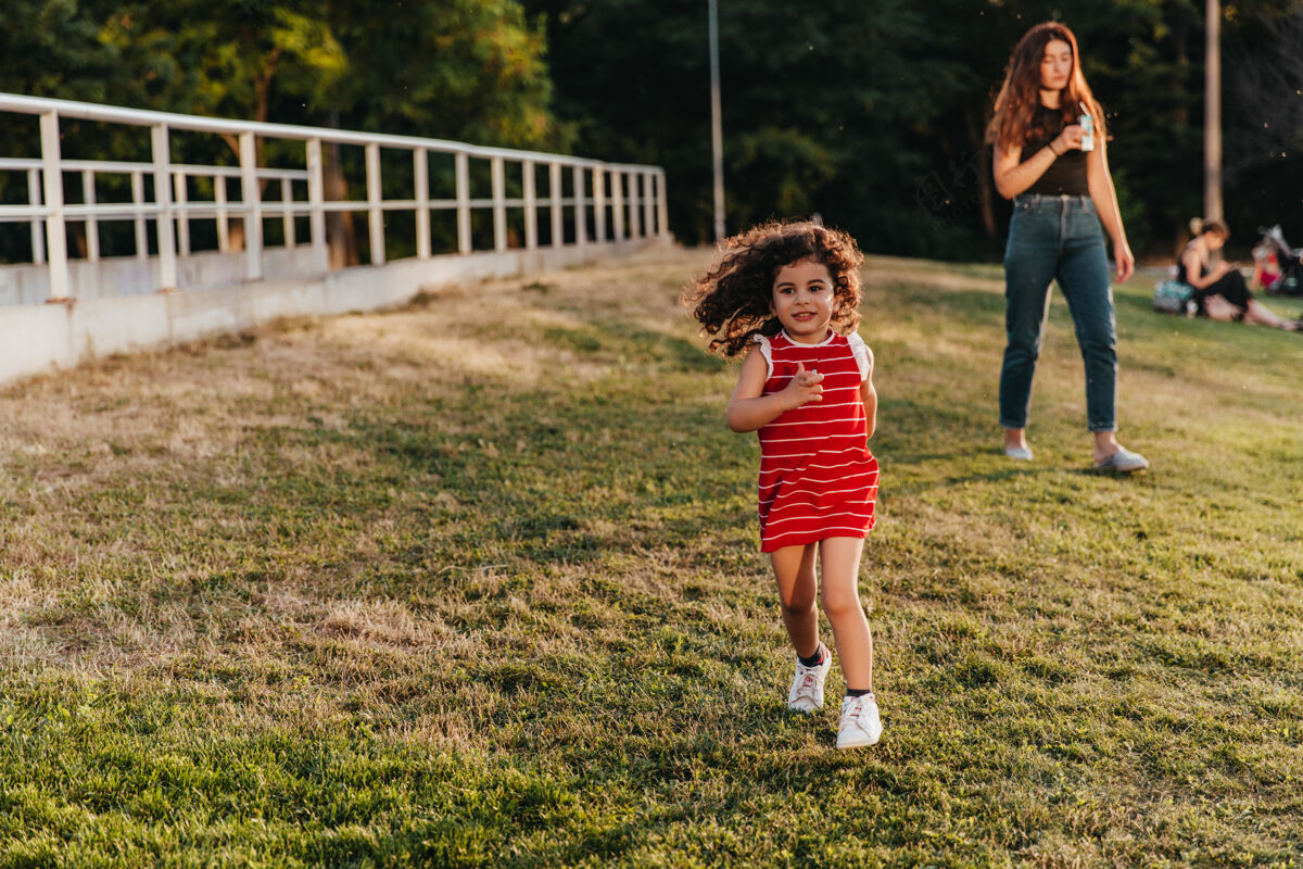 积极穿着红衣服的可爱小女孩在公园里跑步迷人的卷发孩子在草坪上玩耍年轻和平舞蹈