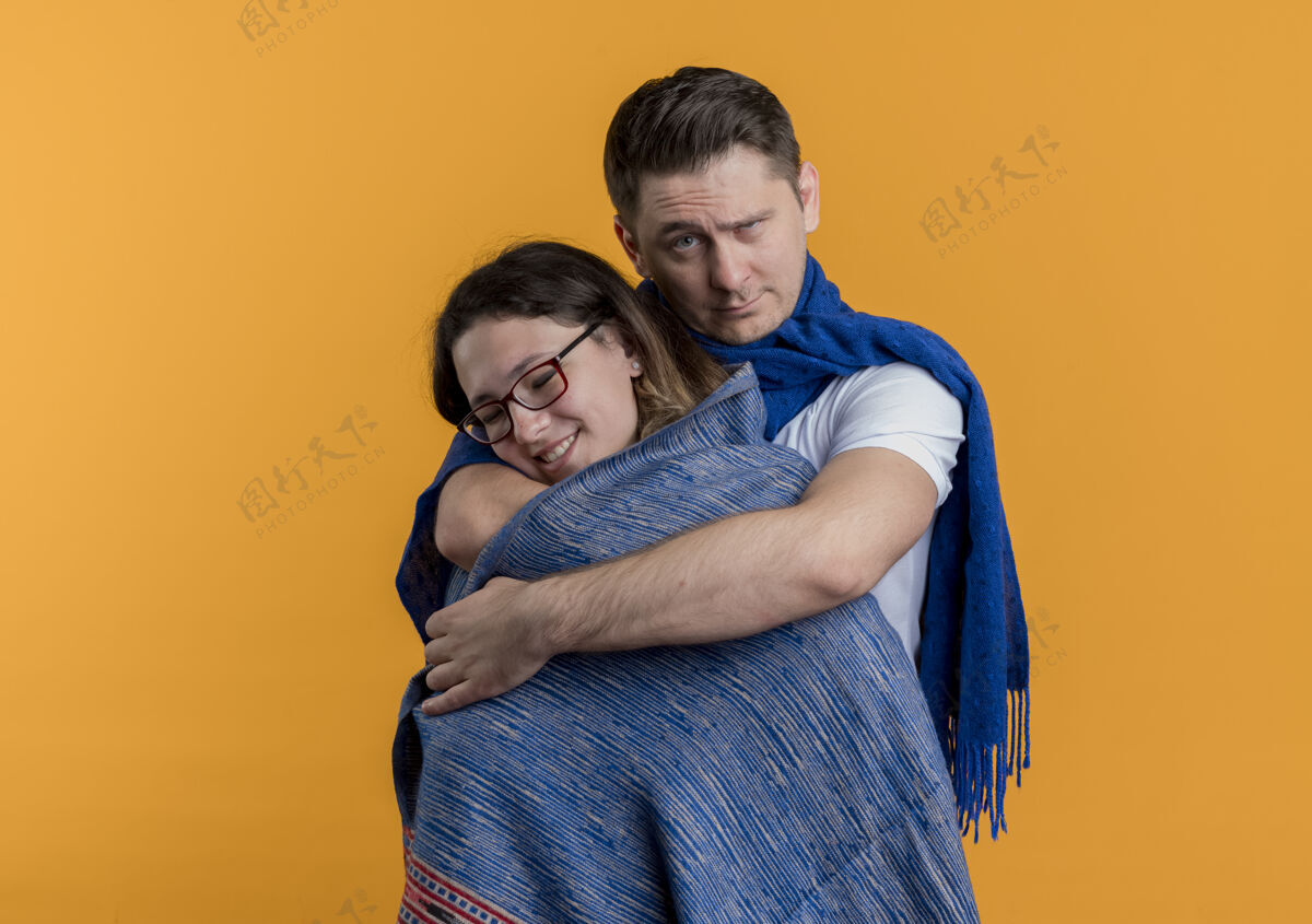 夫妻一对年轻的情侣 一对热恋中的男女 站在橙色的墙上 用一张严肃的脸给女友盖上一条温暖的毯子女人脸毯子