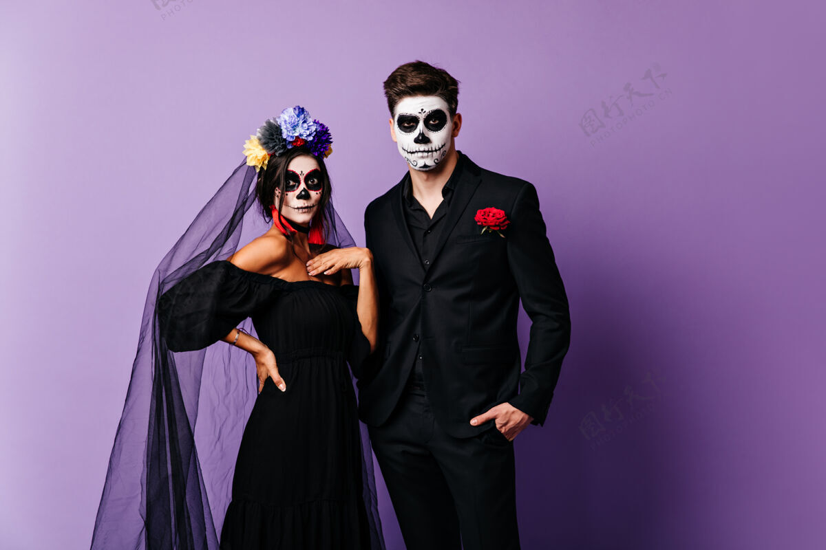 玫瑰万圣节新娘和男友身着经典服装 脸上画着骷髅头形状的惊讶女士的肖像文化节日骷髅