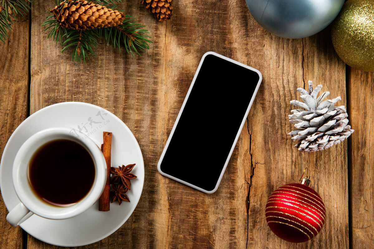 墙壁木质墙壁上的智能手机空白屏幕上有五颜六色的节日装饰 茶水和礼物品牌纸张蓝图