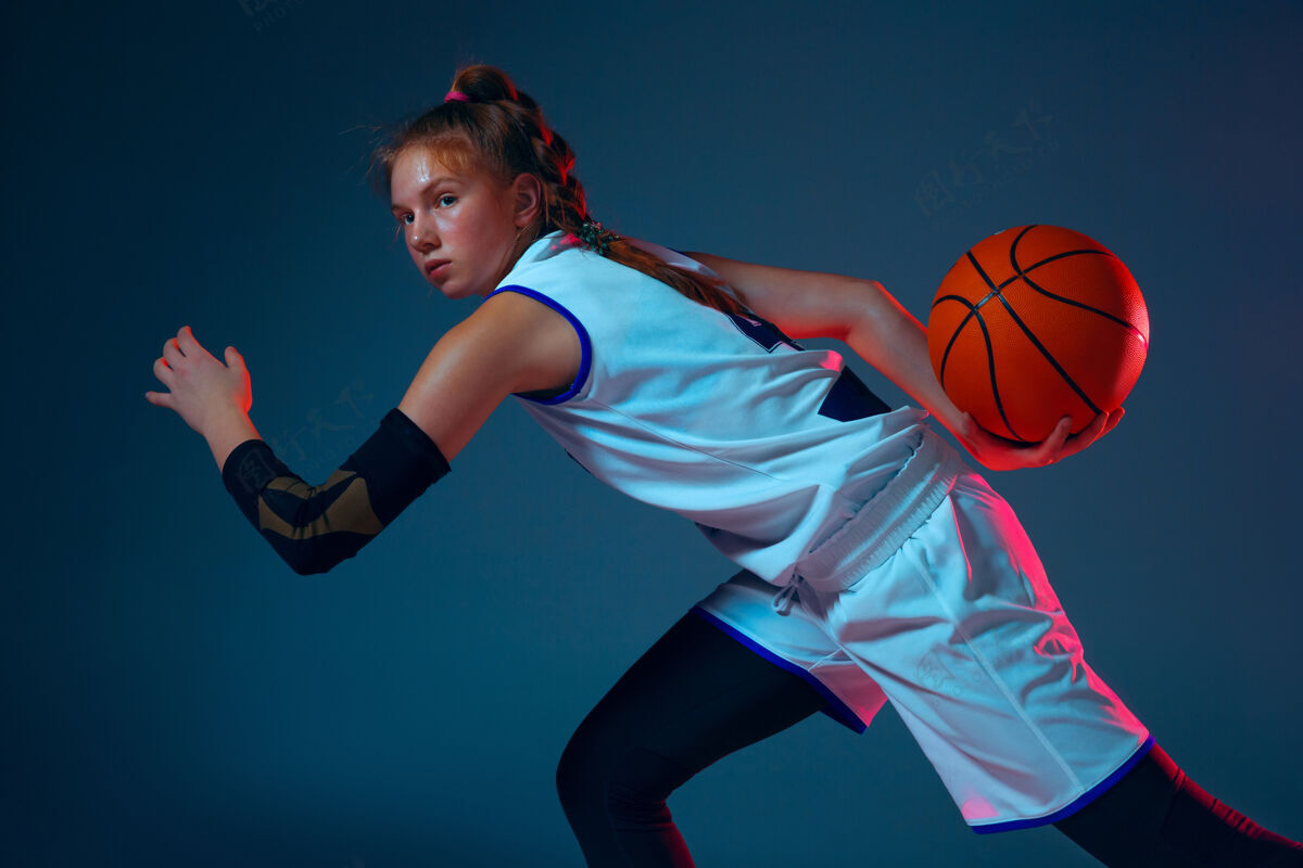 运动员年轻的白人女篮球运动员在霓虹灯下的蓝色墙上健身房动感运动员