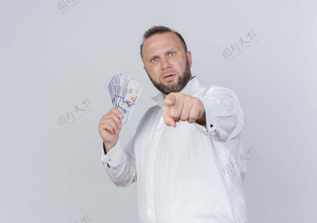 站着留着胡子的男人穿着白衬衫拿着现金藏着钱 用食指指着站在白墙上不高兴的你们胡子目录指点
