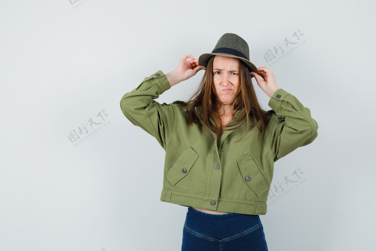 快乐穿着夹克 裤子的年轻女性一边皱眉一边调整着帽子 正面照微笑女人裤子