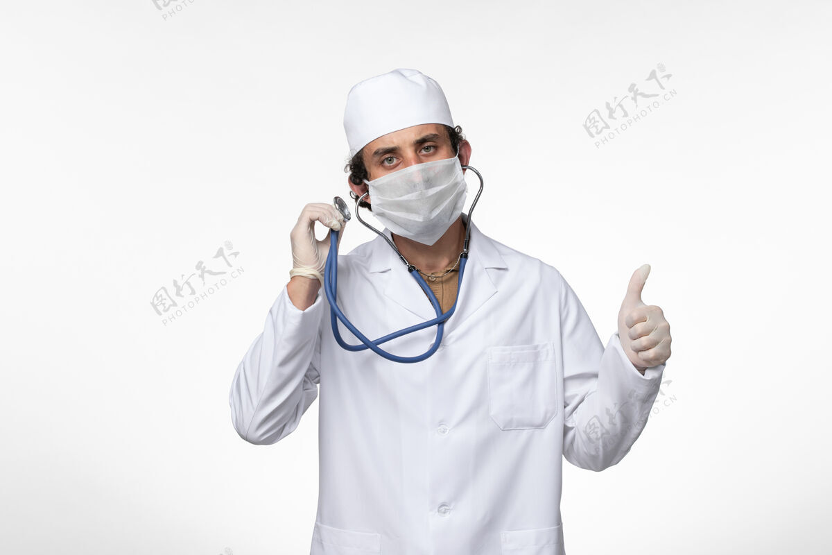 穿着正面图：男医生 穿着医疗服 戴着口罩 以防感染 在白墙上使用听诊器口罩听诊器冠状病毒防护