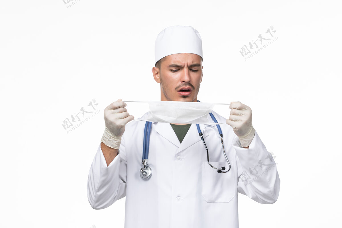 病毒正面图：男医生穿着医疗服 戴着防冠状病毒口罩 白色办公桌上病毒冠状病毒-疾病大流行防护专业人员听诊器