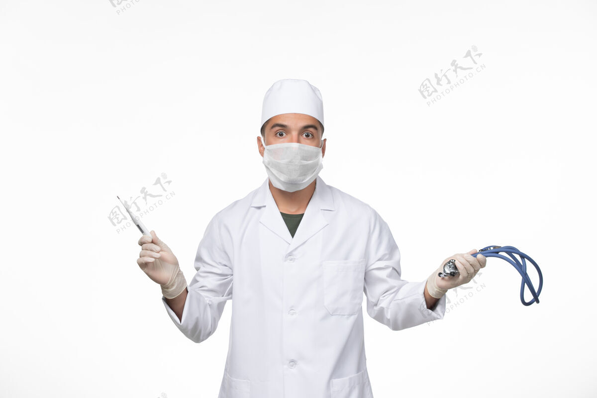 大流行正面图男医生穿着防毒服 戴着防冠状病毒口罩手持听诊器在白墙病毒冠状病毒-疾病大流行正面专业外套