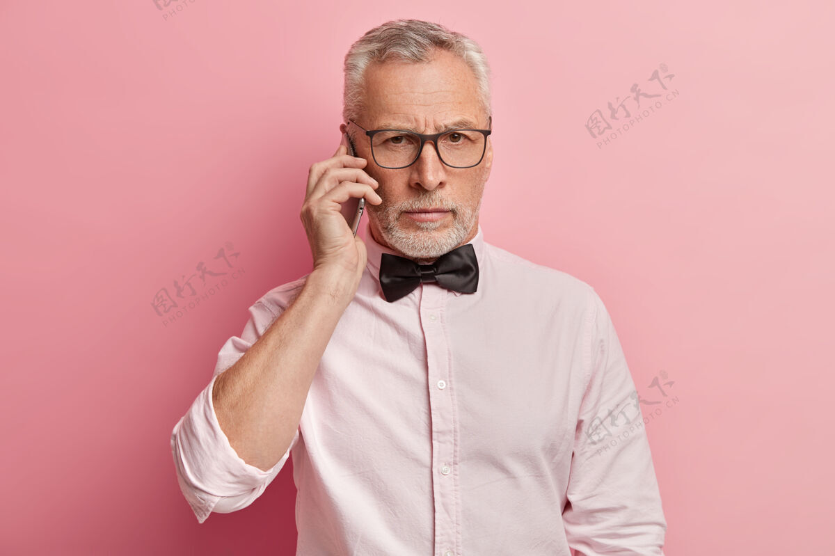 电话资深男子横拍表情严肃地讲电话 把现代手机放在耳边 有对话站立肖像白色