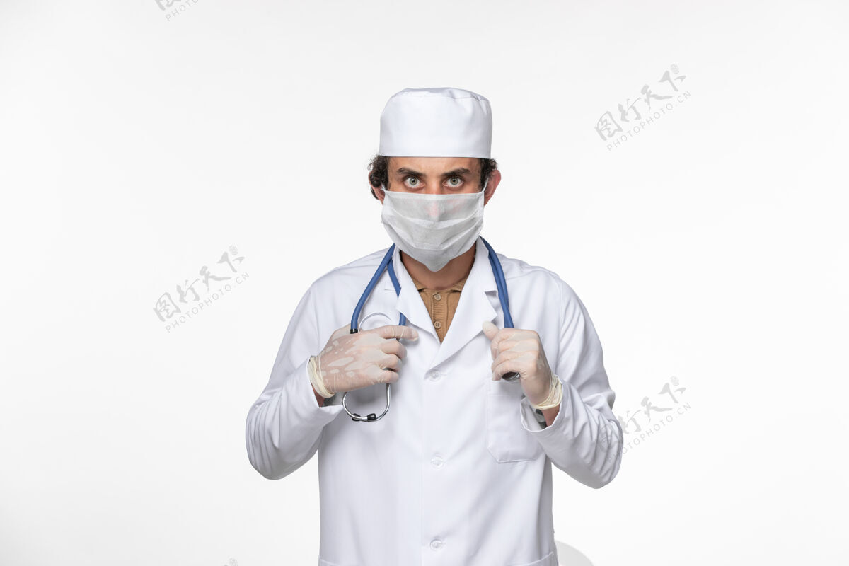 医疗正面图男医生穿着医疗服 戴着无菌口罩 以防白色墙壁上的冠状病毒溅起冠状病毒大流行健康视图听诊器消毒